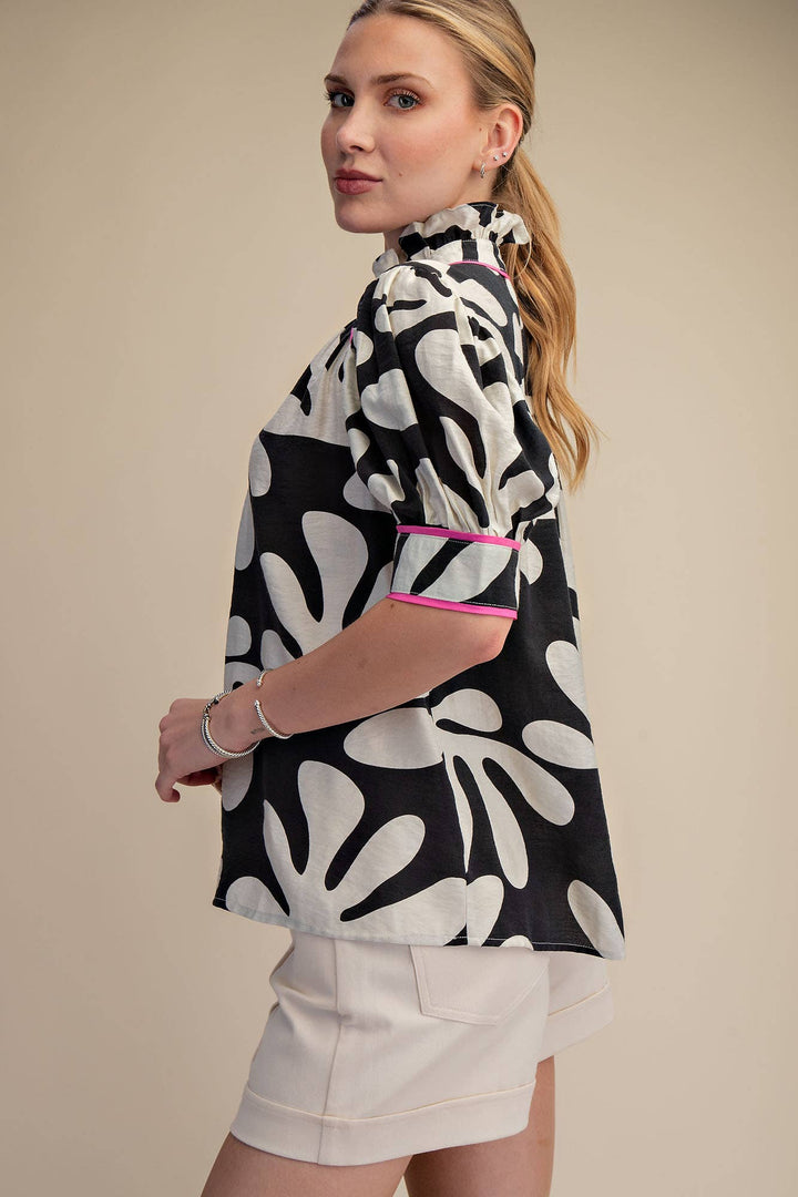 Side view of black and ivory abstract floral blouse with hot pink piping, puff sleeves and ruffled neckline