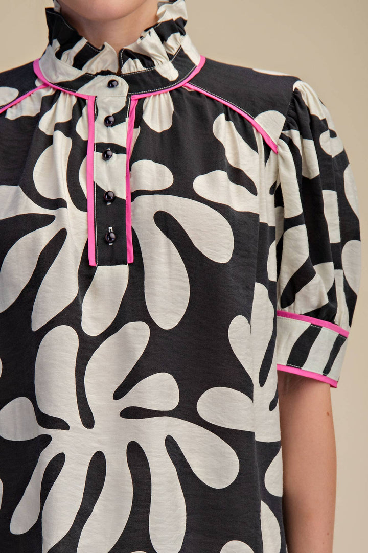 Close-up of black and ivory floral blouse showing hot pink piping, ruffled neckline, black buttons and puff sleeve detail