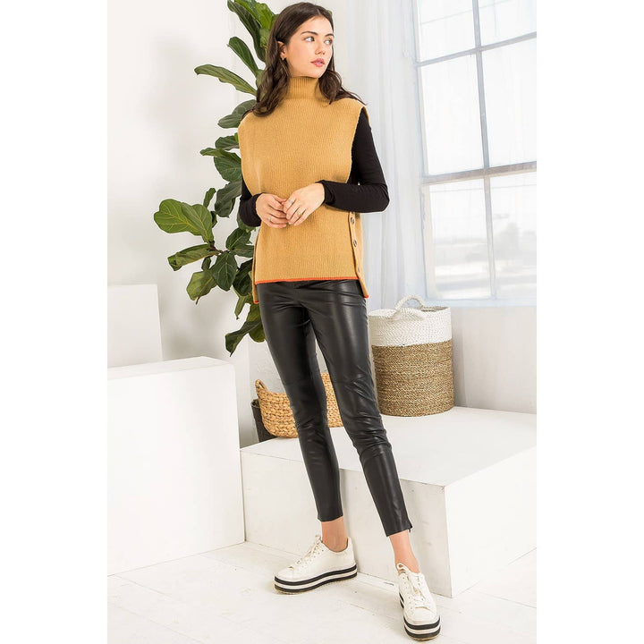 Camel sleeveless sweater vest layered over a black fitted top and styled with black faux leather pants.