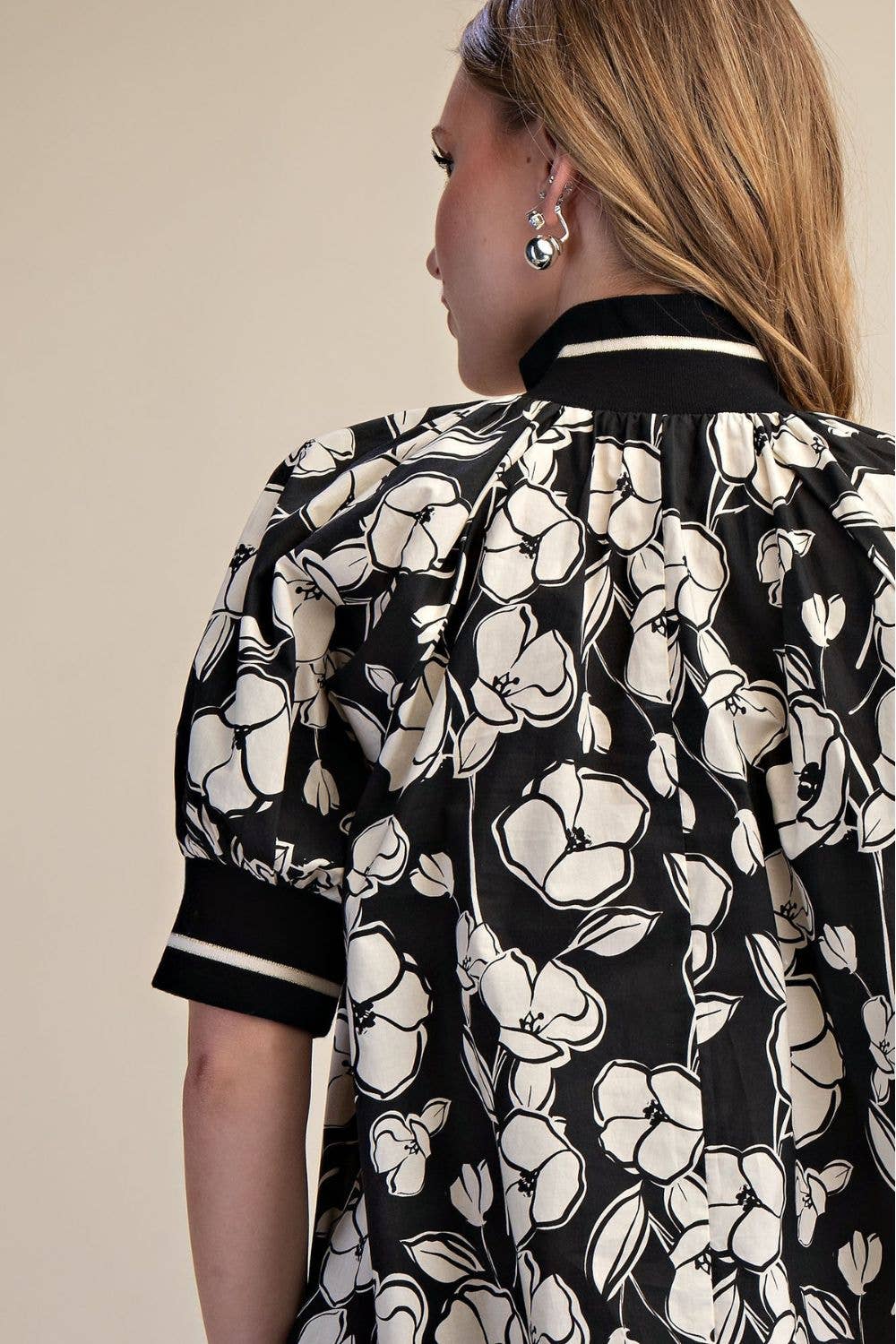 Close-up back view of black and ivory floral dress showing gathered neckline, floral print and striped contrast trim