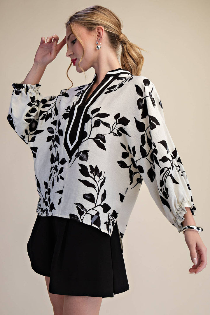 Three-quarter view of black botanical print blouse with relaxed long sleeves and contrast neckline