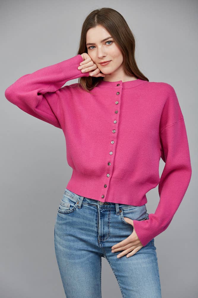 Bright pink button-front cardigan with crew neckline, relaxed fit and long sleeves styled with denim.