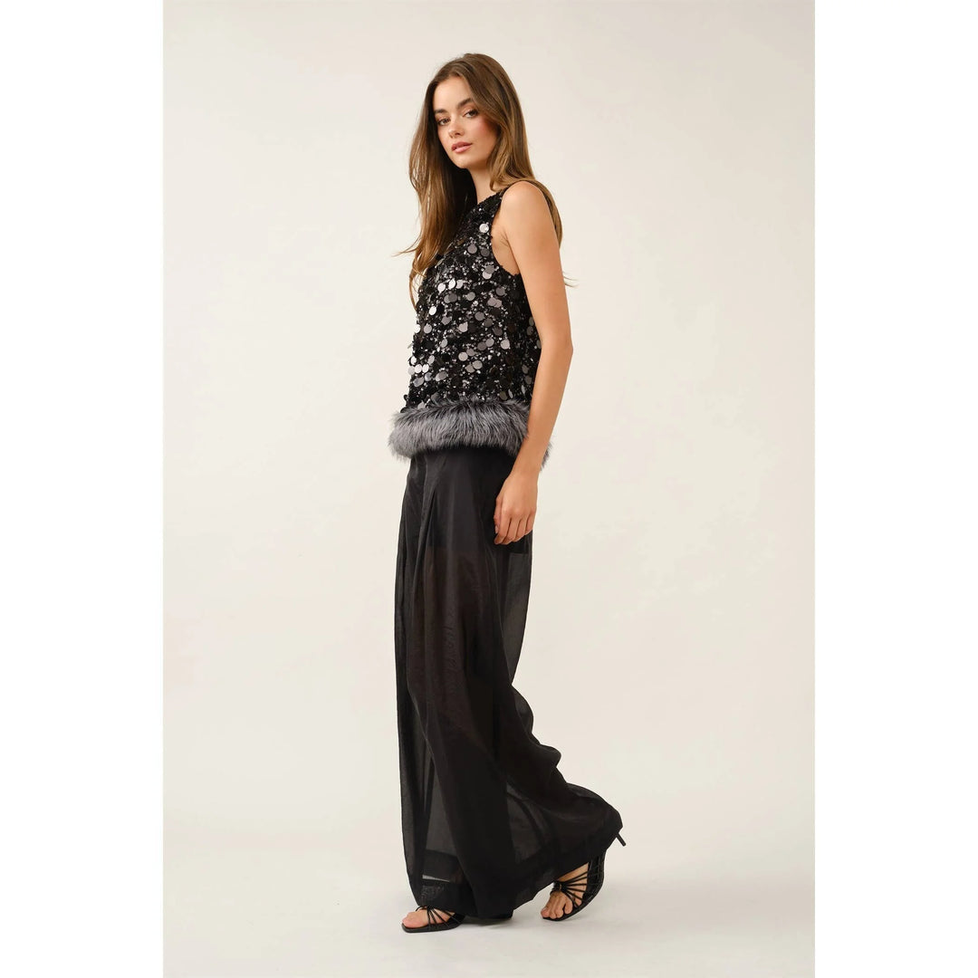 Side view of black sequin faux fur hem top styled with wide-leg black pants